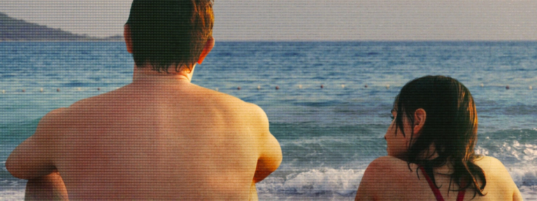 Calum and Sophie sitting together by the sea in Aftersun