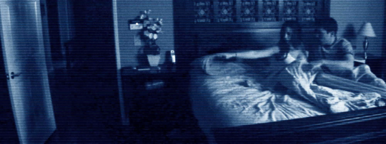 Katie sitting upright in bed in a blue tinted bedroom surveillance camera scene from Paranormal Activity (2009).