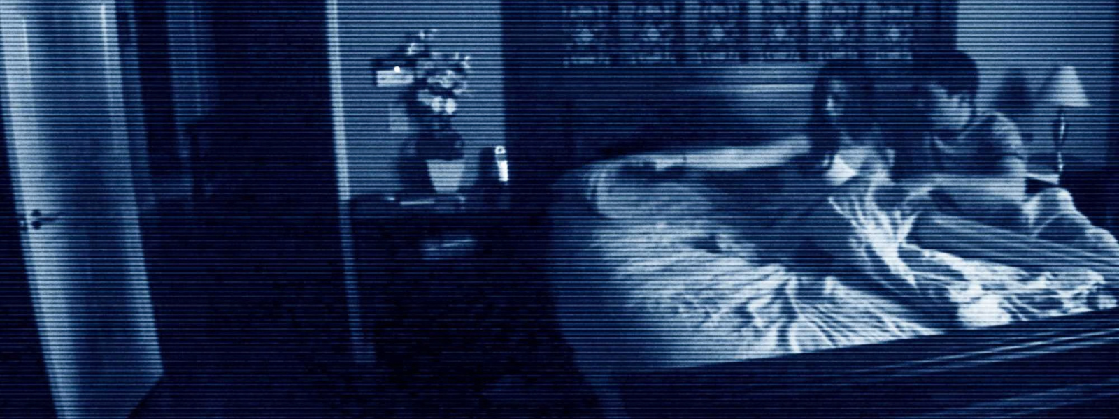 Katie sitting upright in bed in a blue tinted bedroom surveillance camera scene from Paranormal Activity (2009).