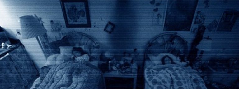 Katie and Kristi sleeping in separate beds in a blue tinted bedroom camera scene from Paranormal Activity 3 (2011).